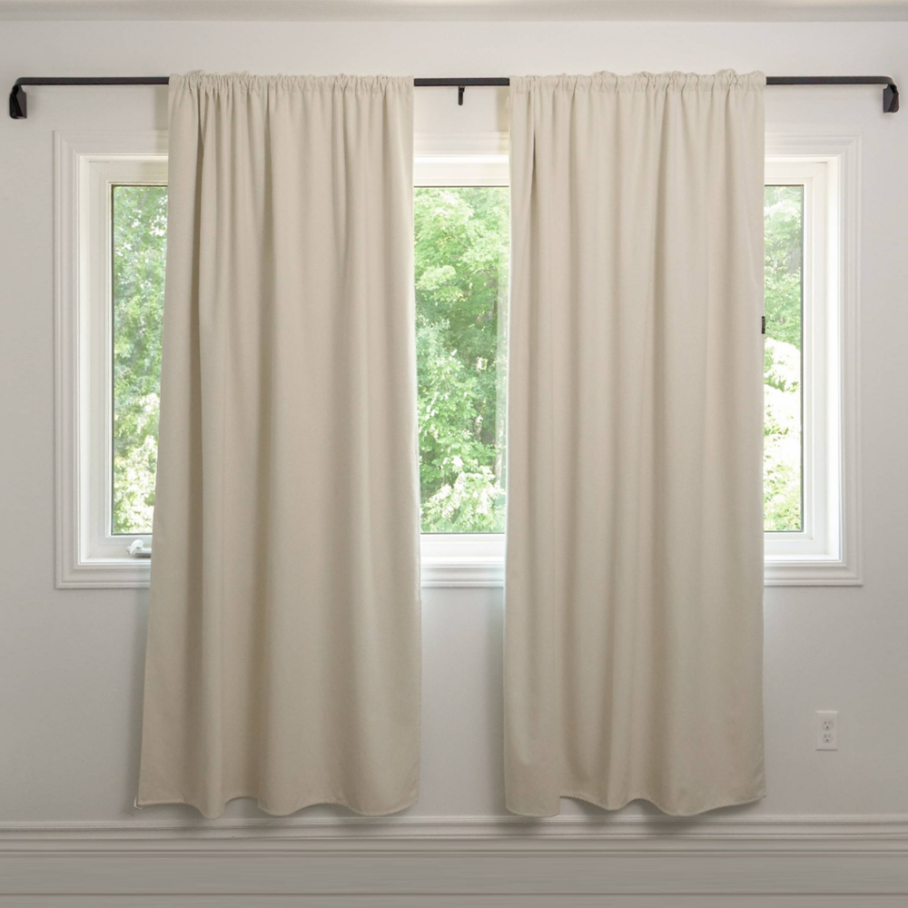 Beige curtain hanging in a room beside a potted palm plant.